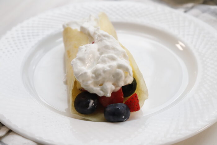 finished breakfast crepes on white plate with berries and cool whip