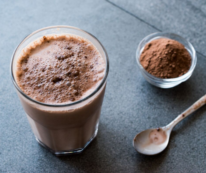 chocolate protein shake in a glass next to spoon