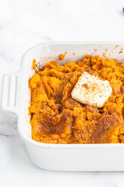 close up of Instant pot mashed sweet potatoes in a casserole dish topped with butter