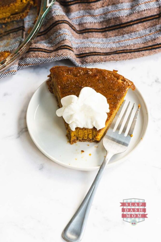 pumpkin pie on a white plate next to a fork with a bite taken out