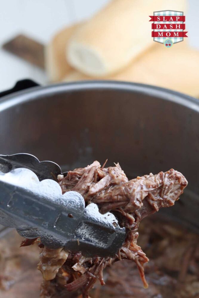 holding shredded french dip meat with tongs over instant pot