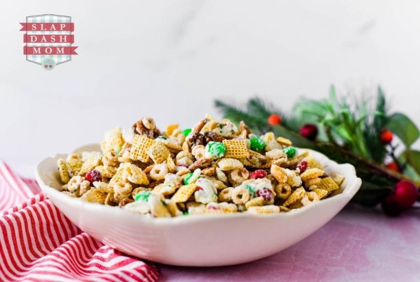 side view of christmas chex mix in a white bowl next to greenery